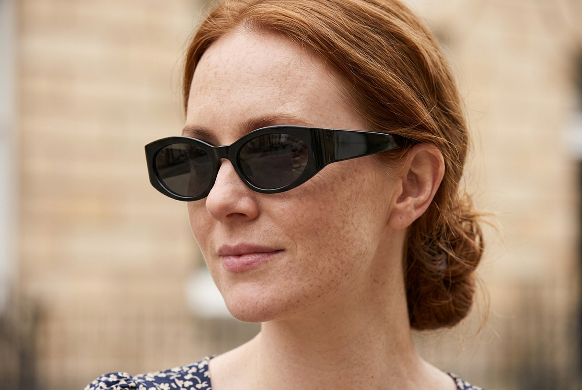 Close-up of a woman wearing glossy black cat-eye sunglasses with dark grey lenses and broad sculpted temples