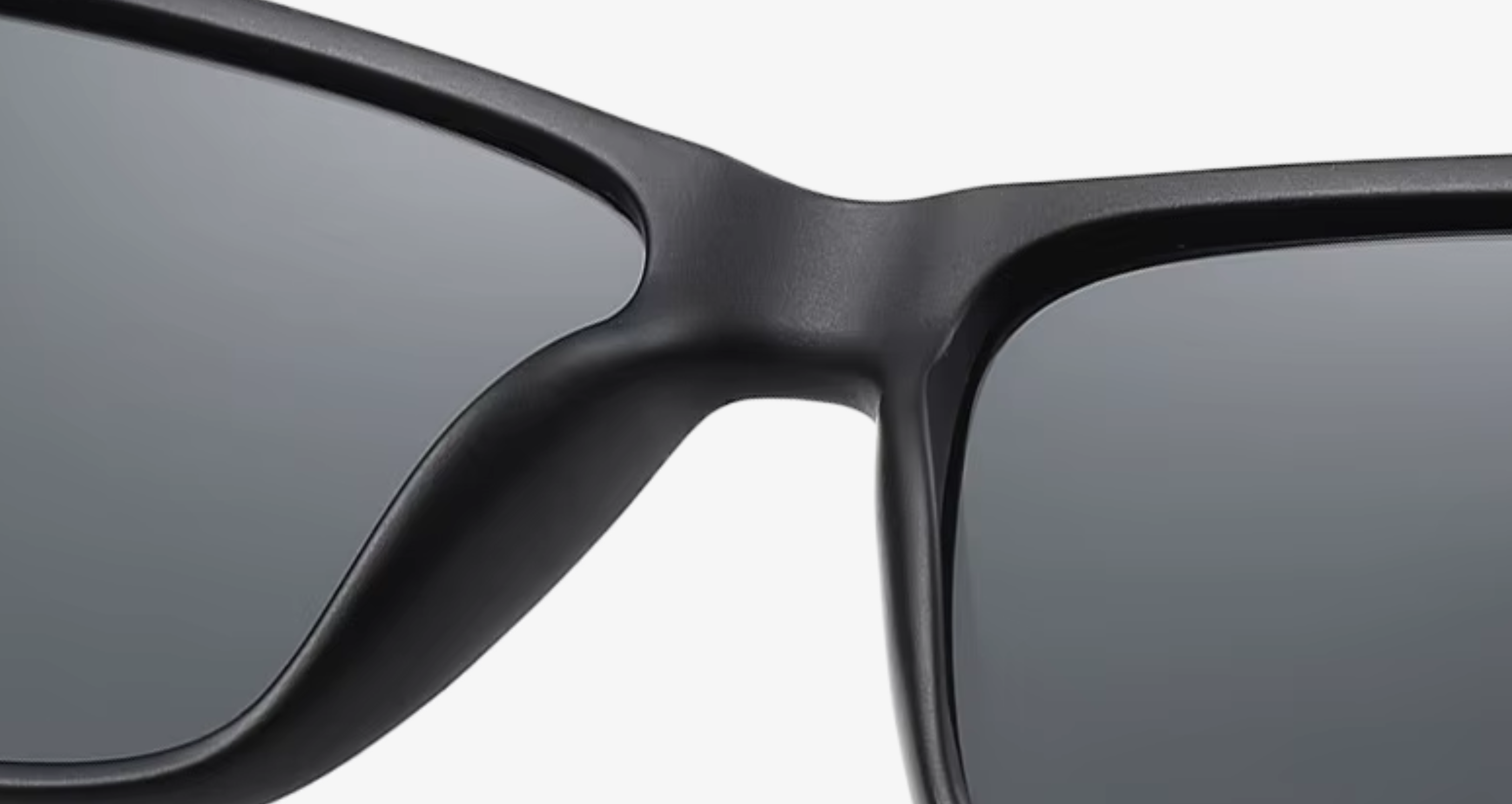 Close-up of a black sunglasses frame showing the bridge and part of the dark tinted lenses against a light gray background.