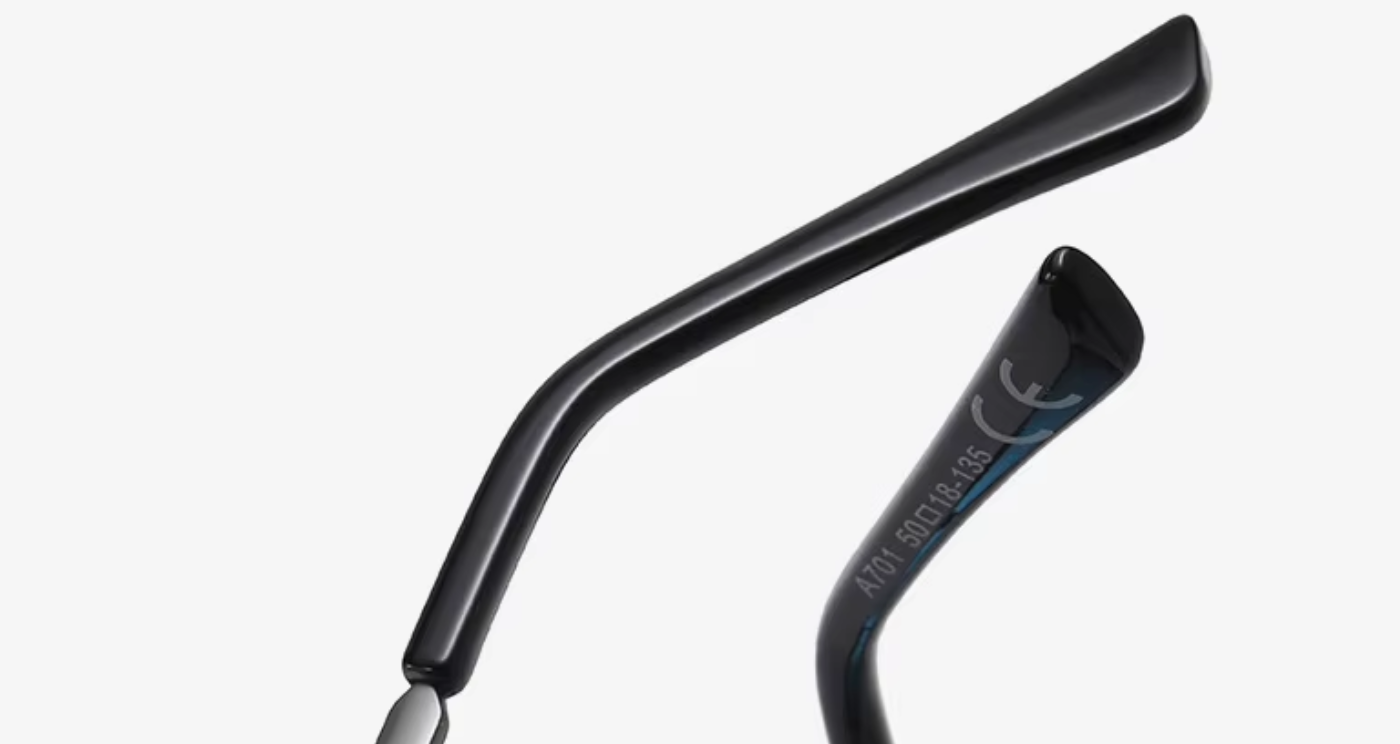Close-up of black metal eyeglass temple arms on a light gray background, with one arm showing the text 'ANTI SCUFFLE'.