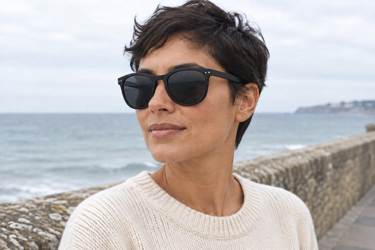 Woman by the seaside wearing Convert II foldable sunglasses with black frames and dark lenses